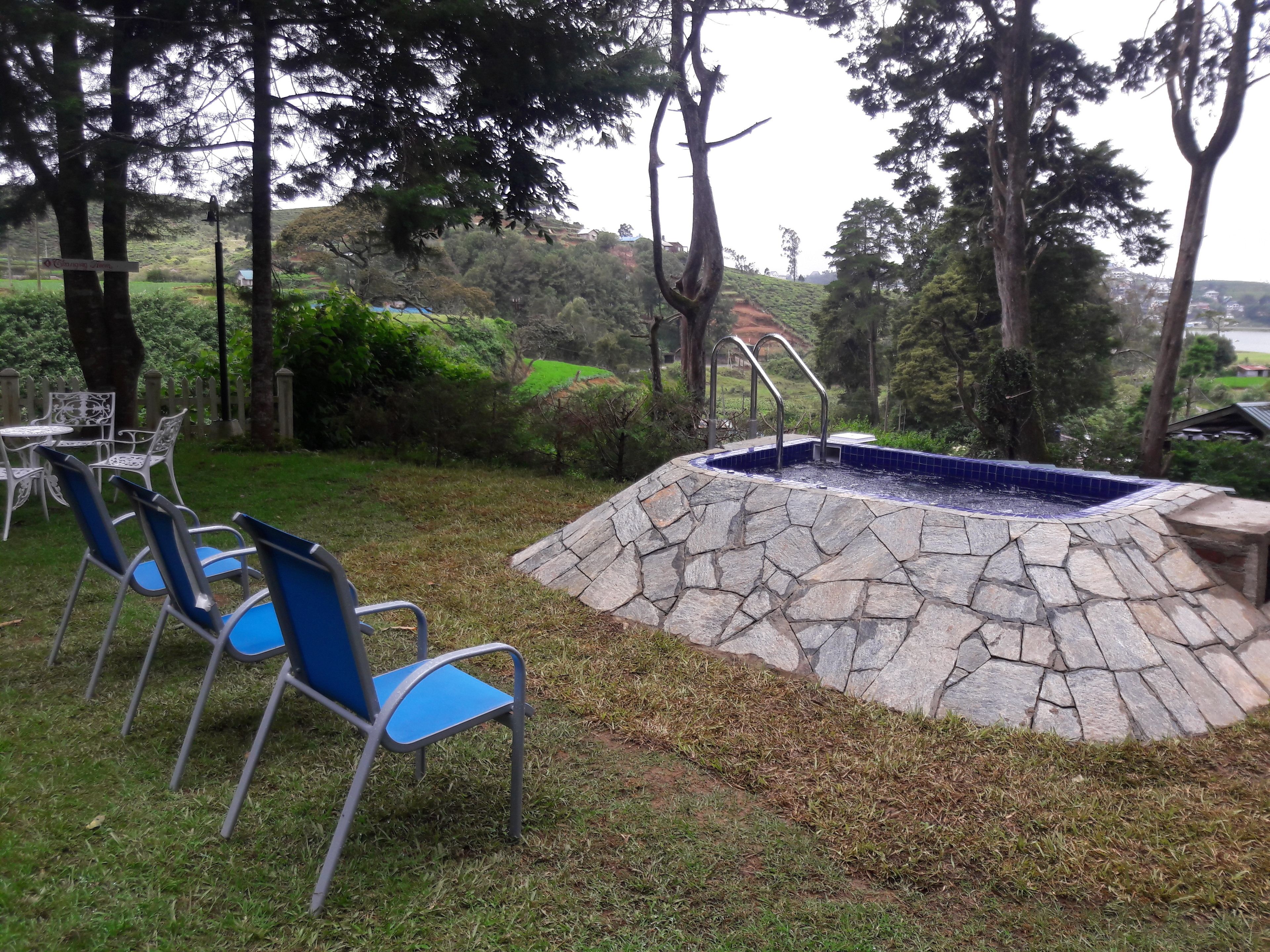 Una piscina de piedra con un muro de piedra, rodeada de sillas azules y una valla blanca.