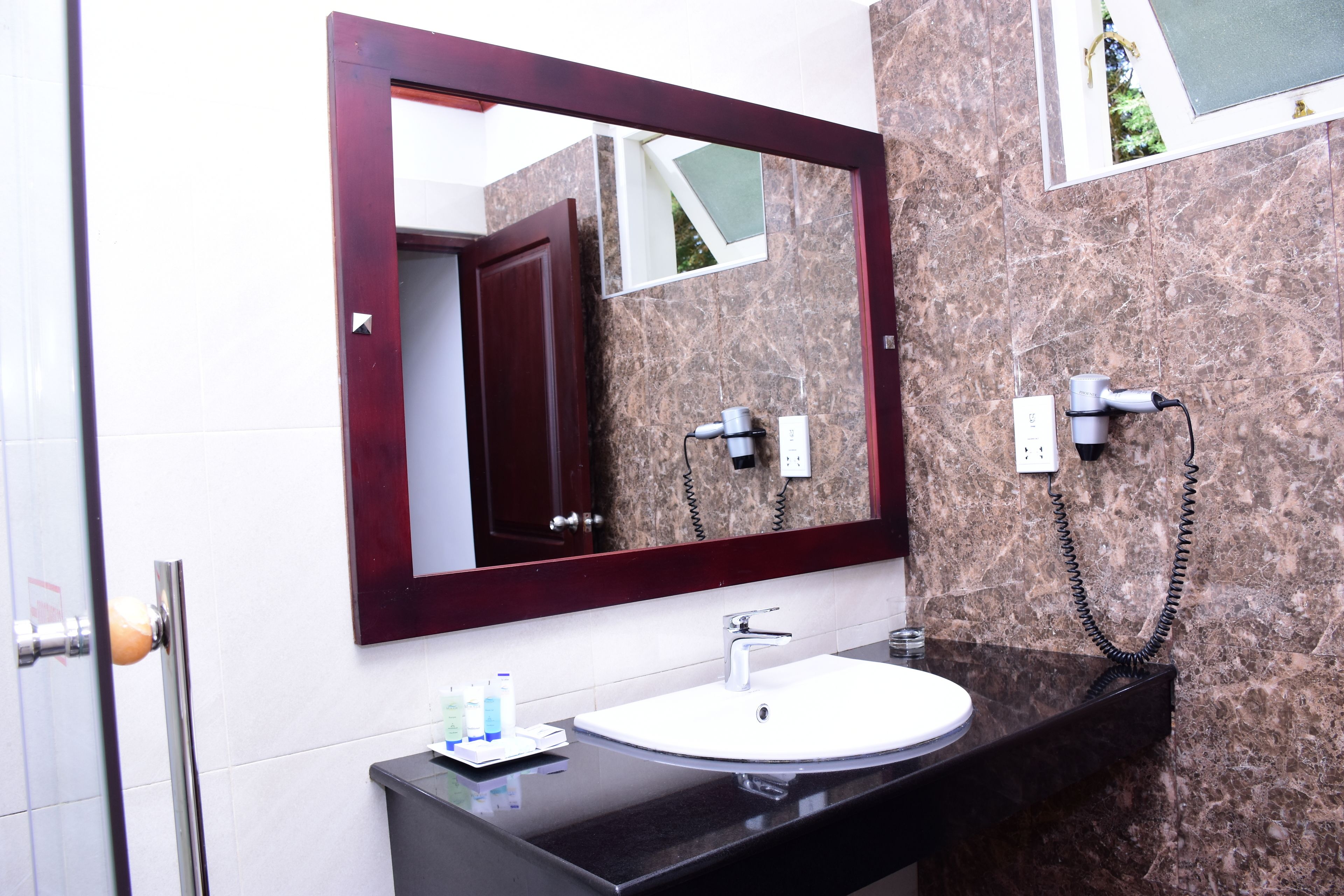 A bathroom with a marble wall, a white sink, a dark countertop, and a large mirror with a wooden frame.