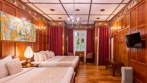 A hotel room with two beds, a painting, a chandelier, and a television. - Mirage Kings Cottage (Nuwara Eliya)