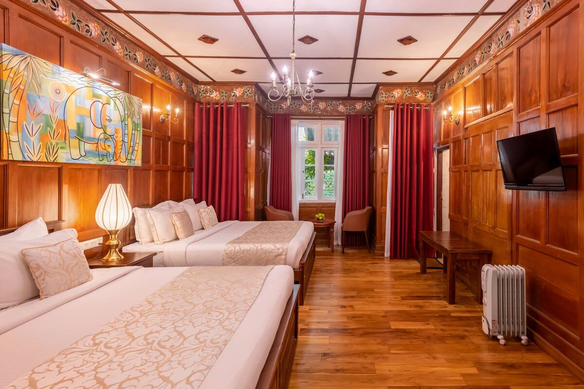 Ein Hotelzimmer mit zwei Betten, einem Gemälde, einer Chandelüster und einem Fernseher.