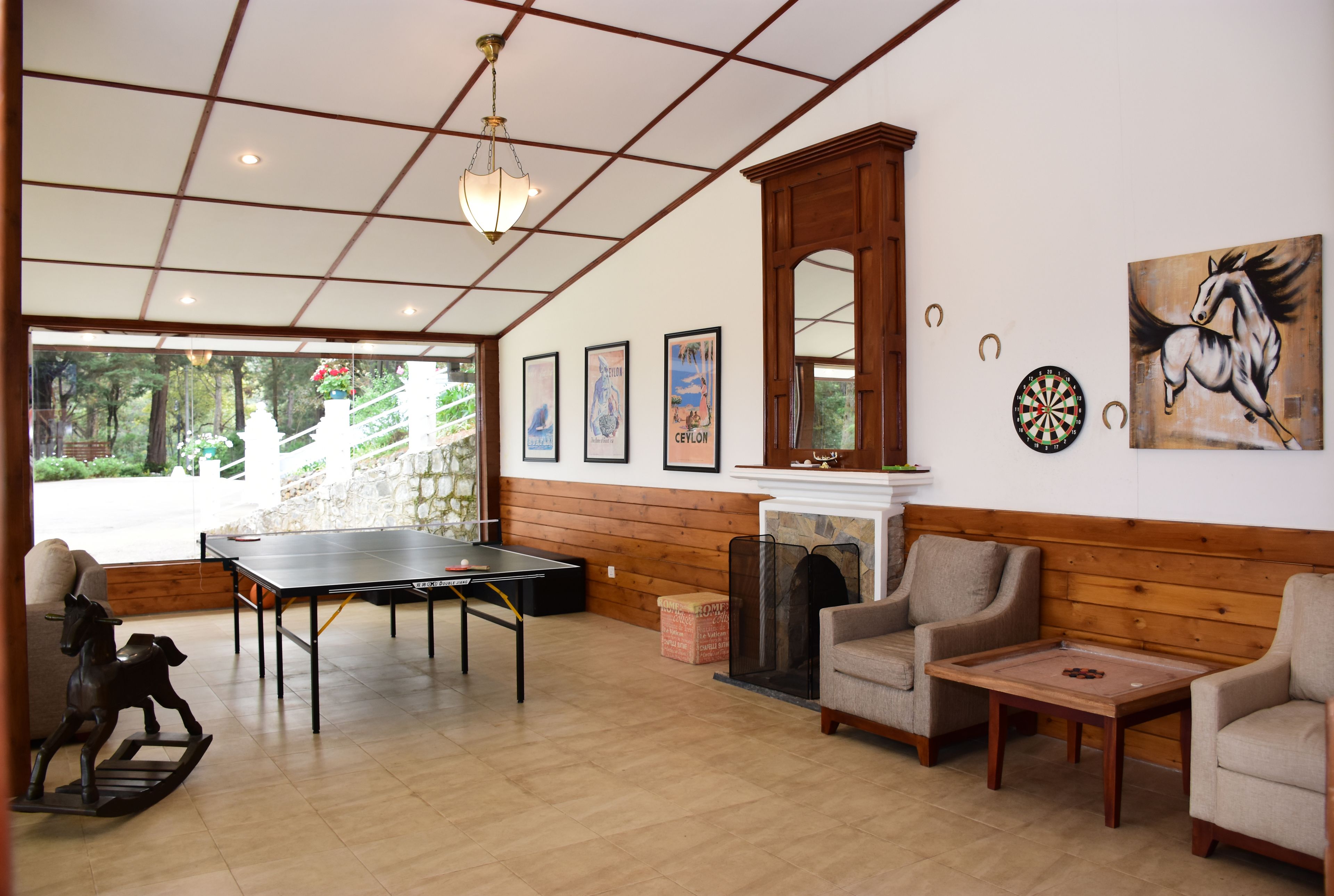 A room with a ping pong table, two armchairs, a fireplace, and framed artwork on the wall.