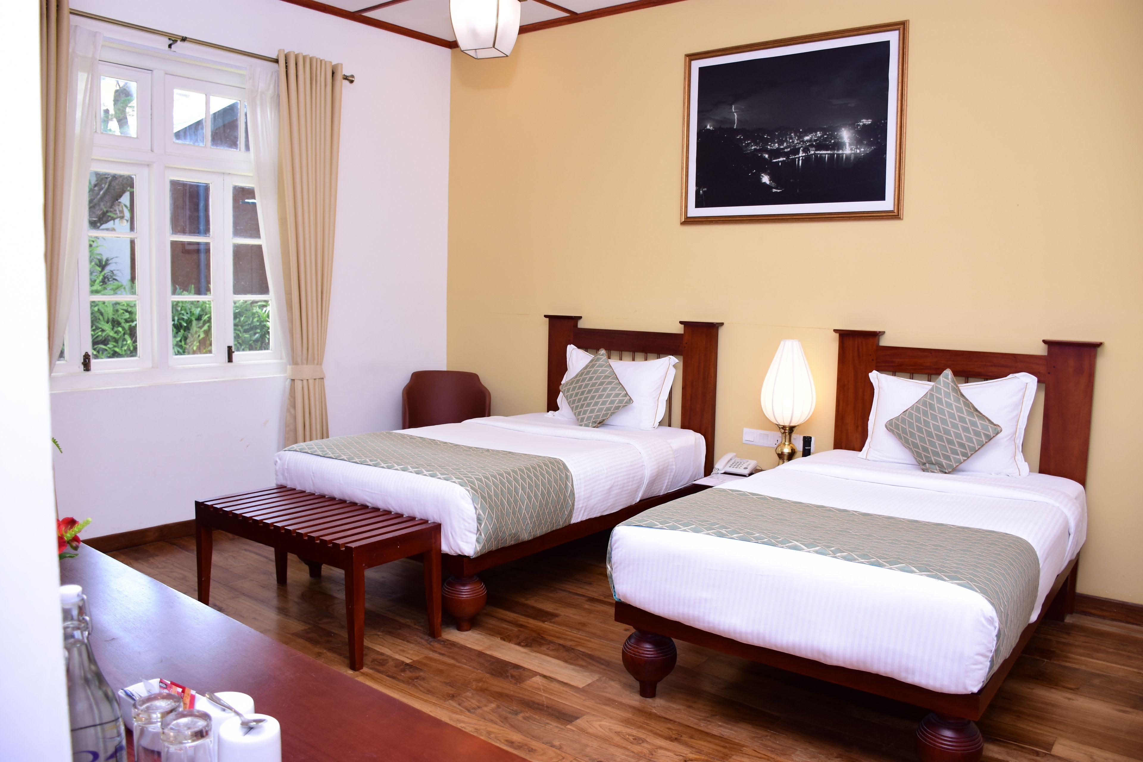 A hotel room with two beds, wooden flooring, a night view poster, and a window with curtains.