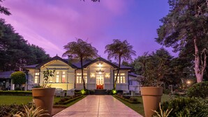 A two-story house with a well-lit entrance, surrounded by a garden with potted plants and a pathway leading to the front door. - Mirage Kings Cottage (Nuwara Eliya)