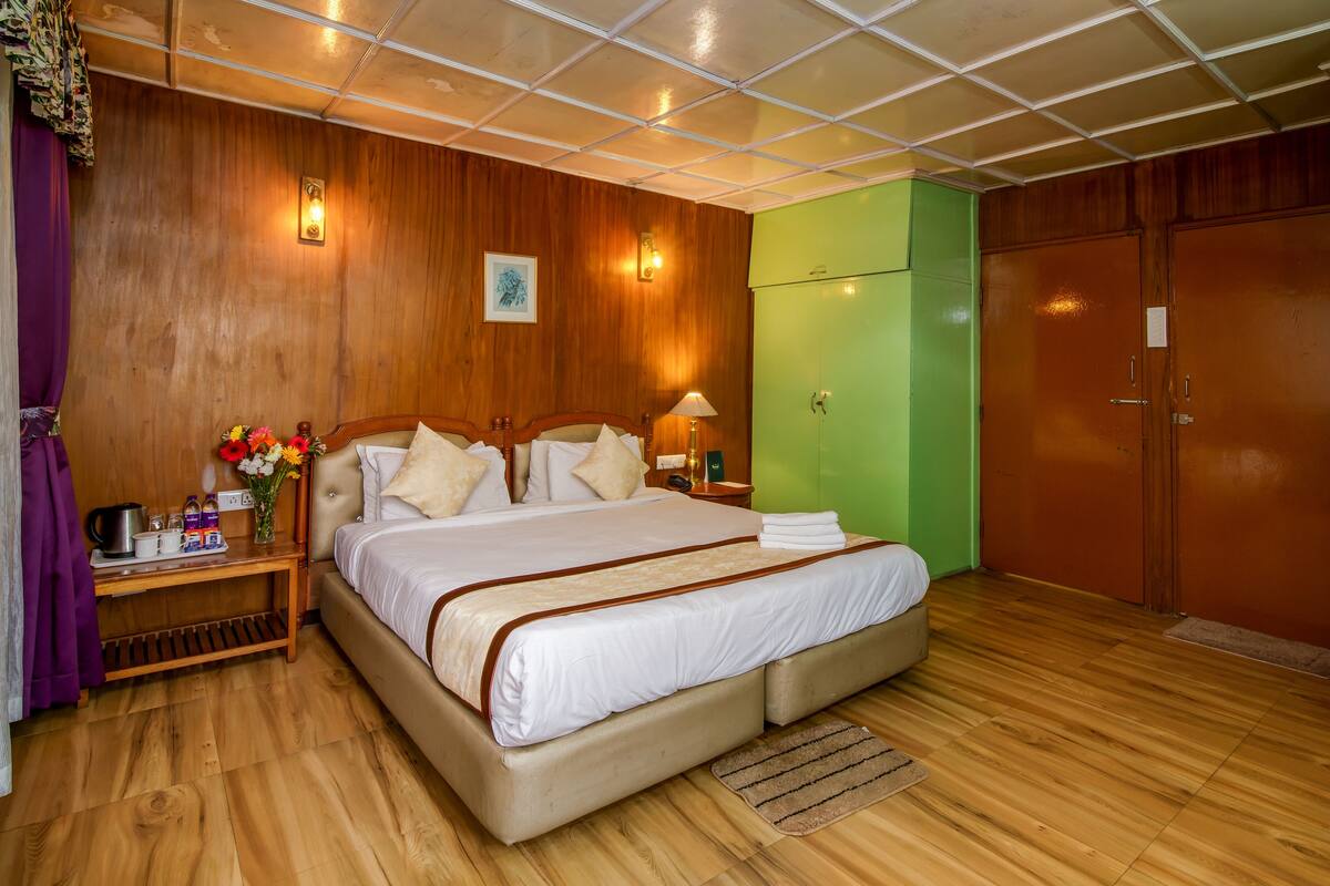 Una habitación de hotel con una cama grande, paneles de madera, un armario verde y suelo de madera.