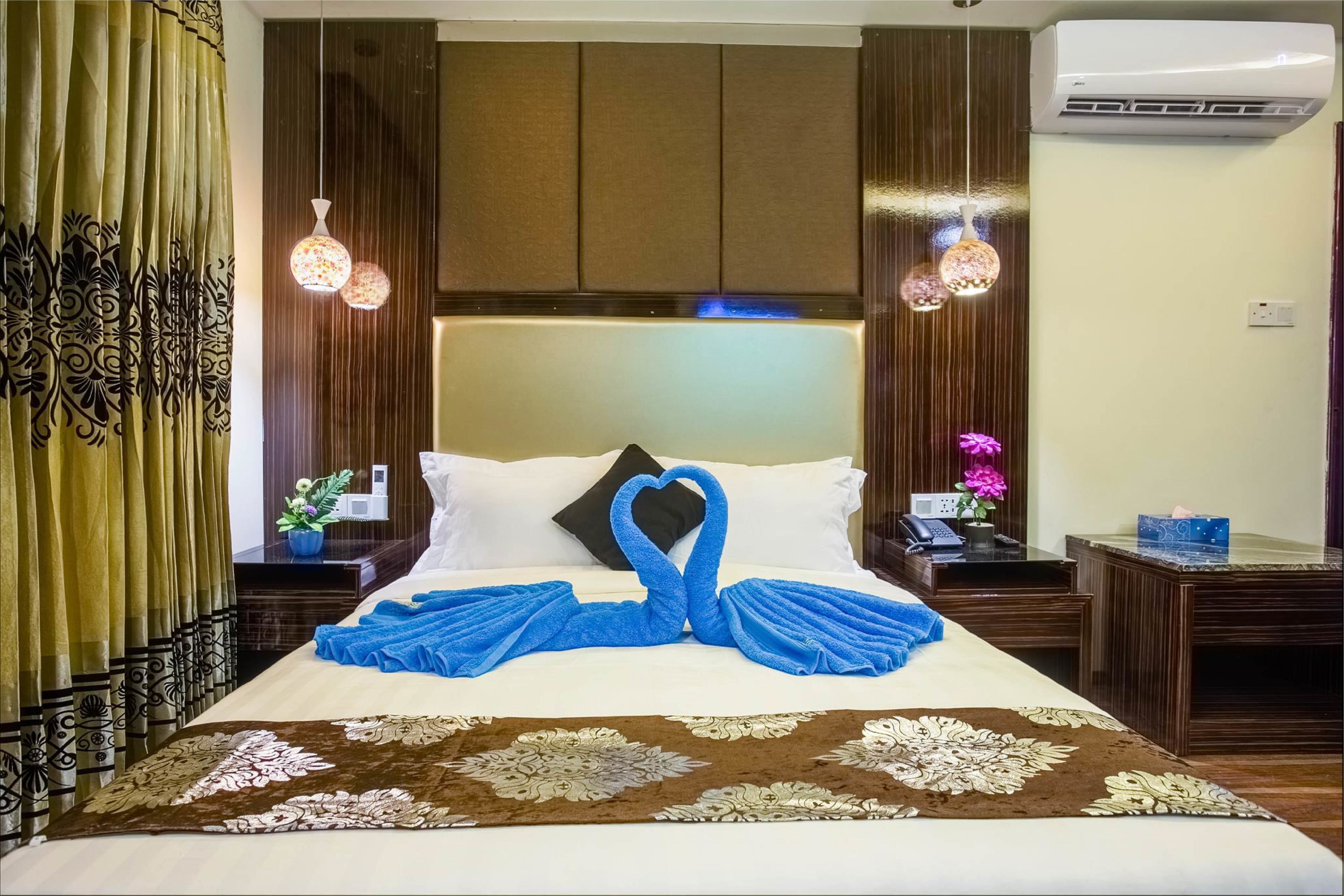 A neatly made bed with a heart-shaped towel arrangement, a floral-patterned rug, and a wooden headboard.