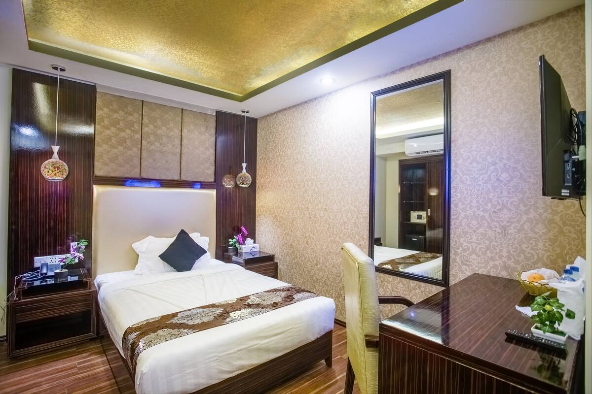 A hotel room with a large bed, a desk, a chair, a TV, and a mirror.
