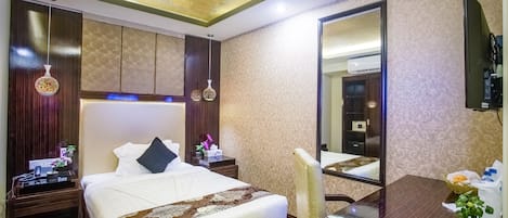A hotel room with a large bed, a desk, a chair, a TV, and a mirror.