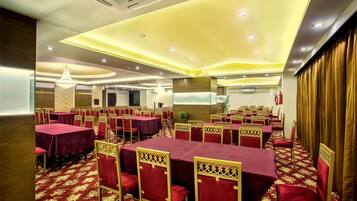 A banquet hall with tables covered in red tablecloths and gold chairs, arranged in rows.