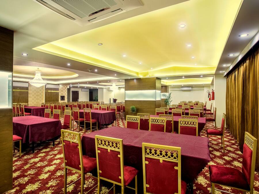 A banquet hall with tables covered in red tablecloths and gold chairs, arranged in rows.