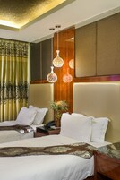 Habitación de hotel con dos camas, cabecero de madera, un jarrón decorativo con flores y lámparas colgantes.