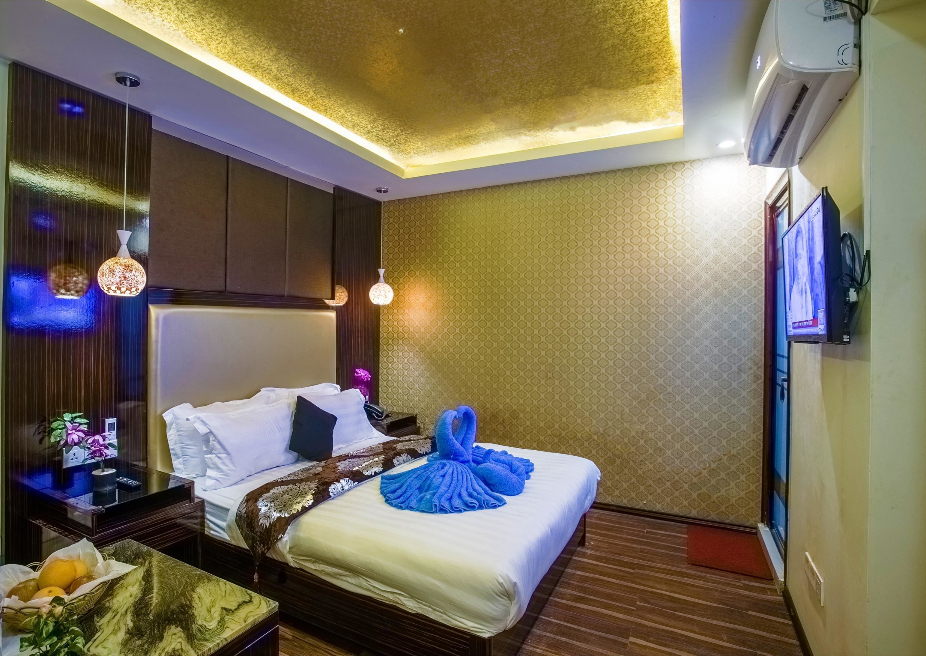 Una habitación de hotel con una cama, mesitas de noche, un televisor y una lámpara en el techo.