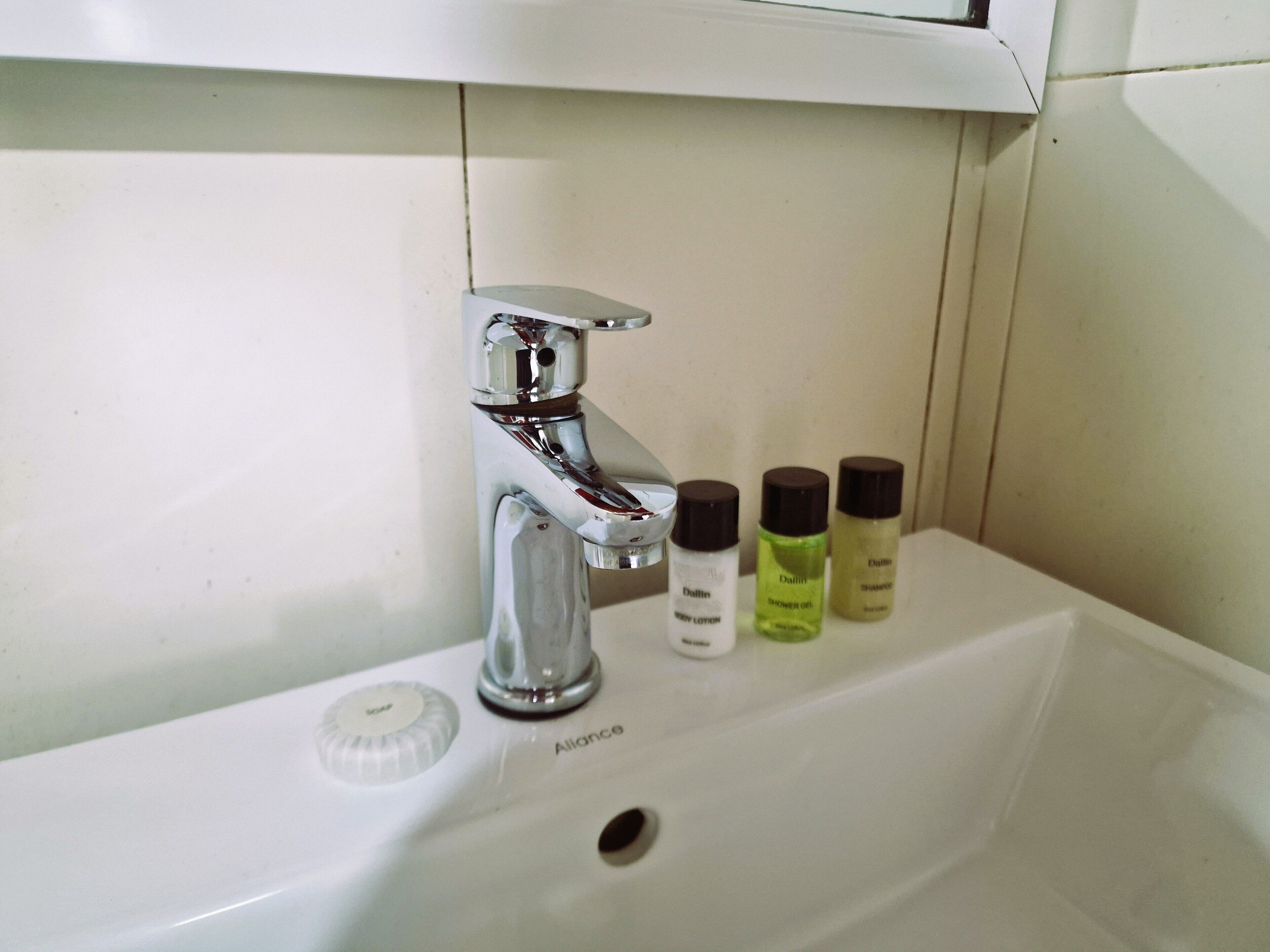 A bathroom sink with a chrome faucet, a soap dispenser, and three bottles of shower gel.