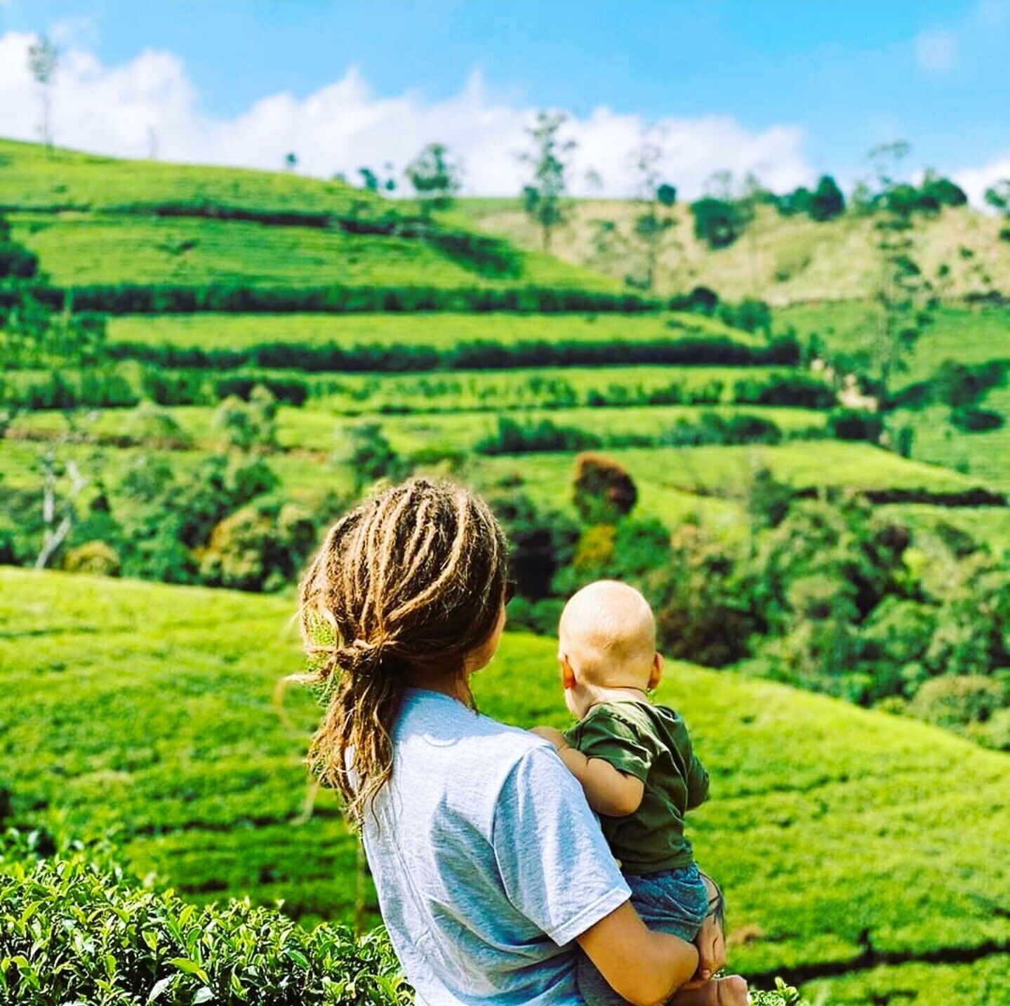 A person holding a child overlooking a green hilly landscape.