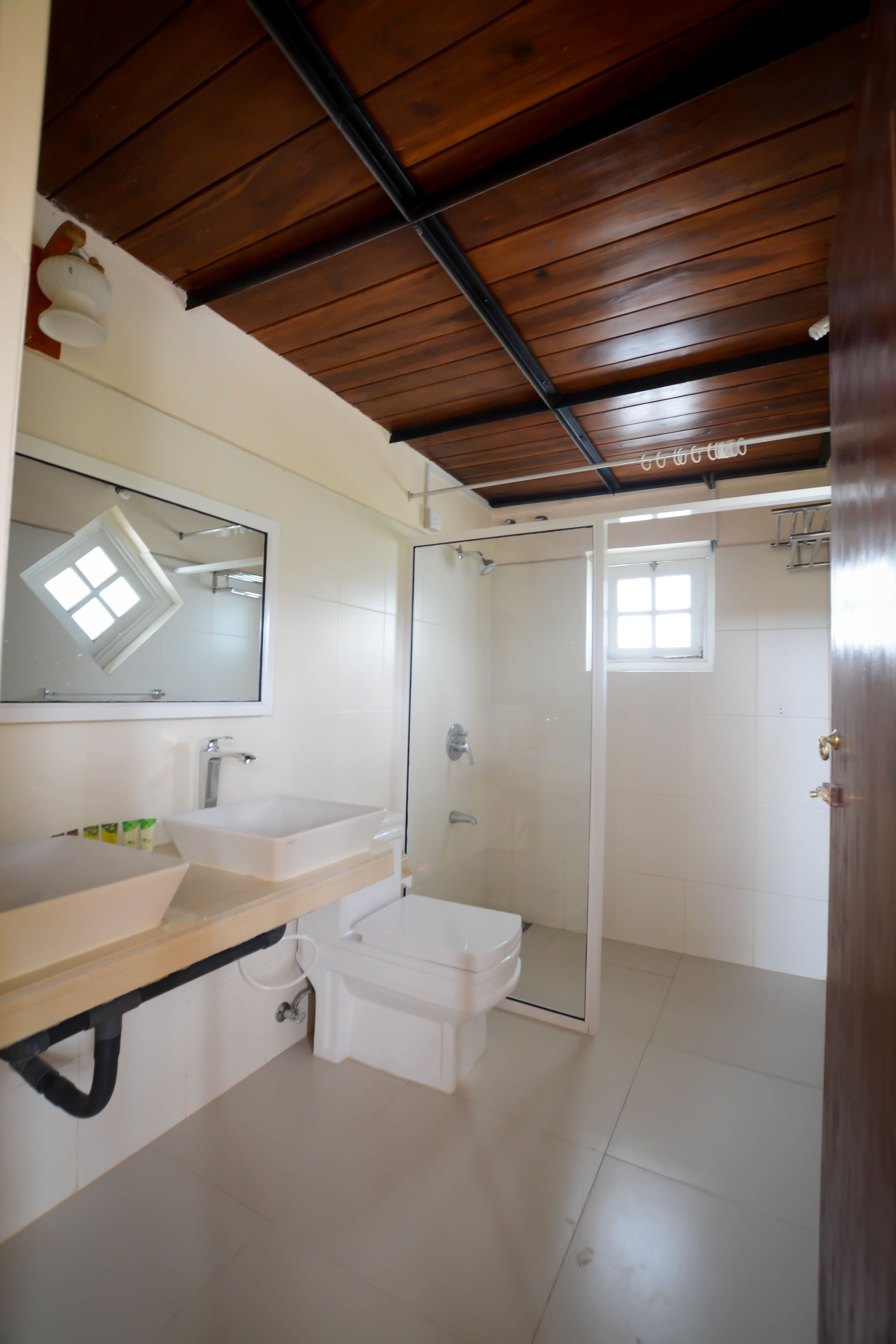 Un baño con techo de madera, un lavabo blanco, un espejo y una cabina de ducha.