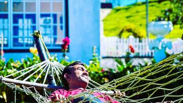A person relaxing in a hammock outdoors with a house and garden in the background.