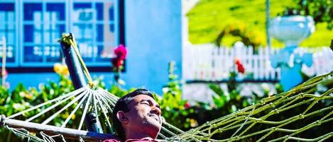 A person relaxing in a hammock outdoors with a house and garden in the background.