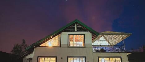A two-story house with a green roof and multiple windows, illuminated at night.
