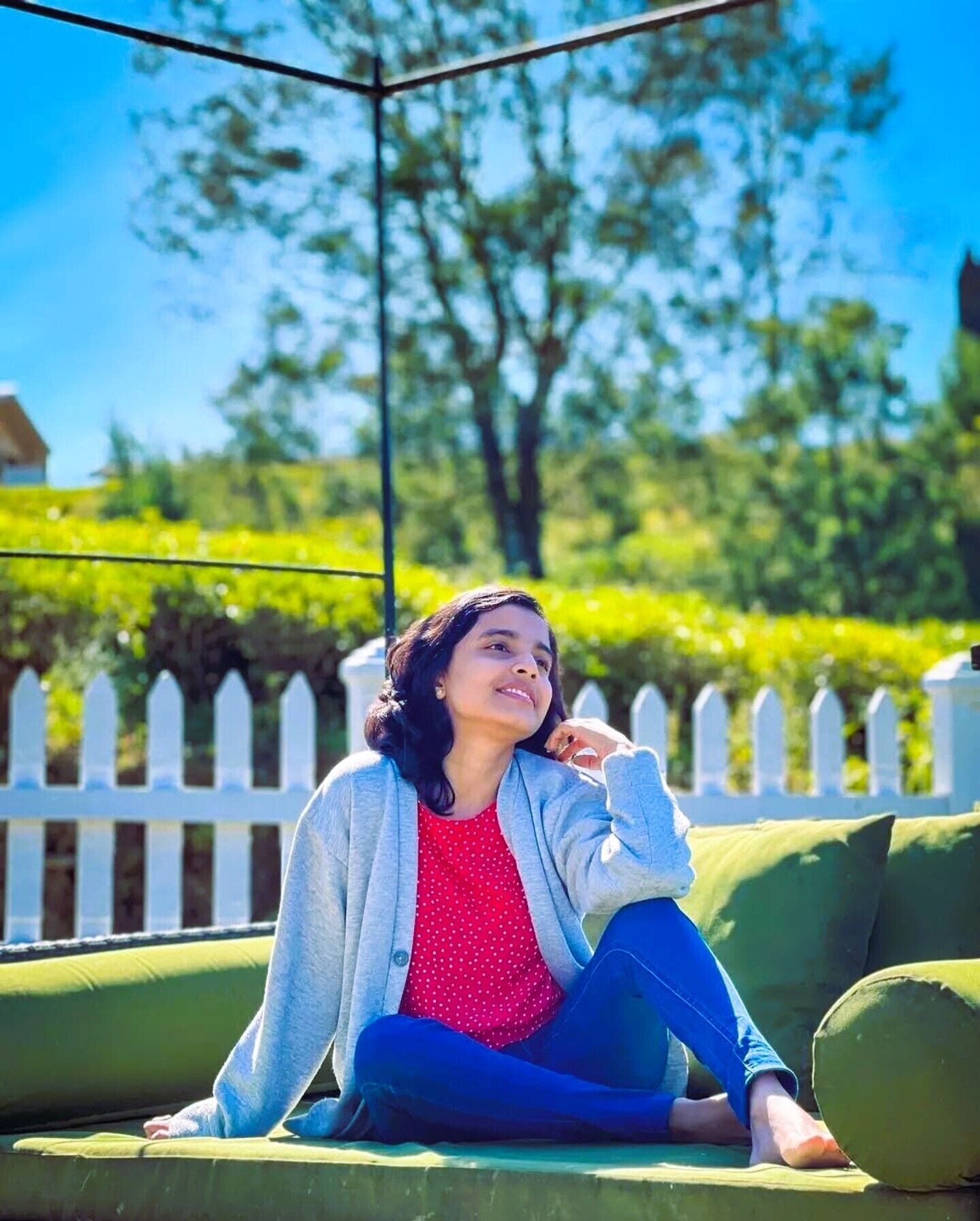 A person sitting on a green outdoor sofa with a white picket fence in the background.
