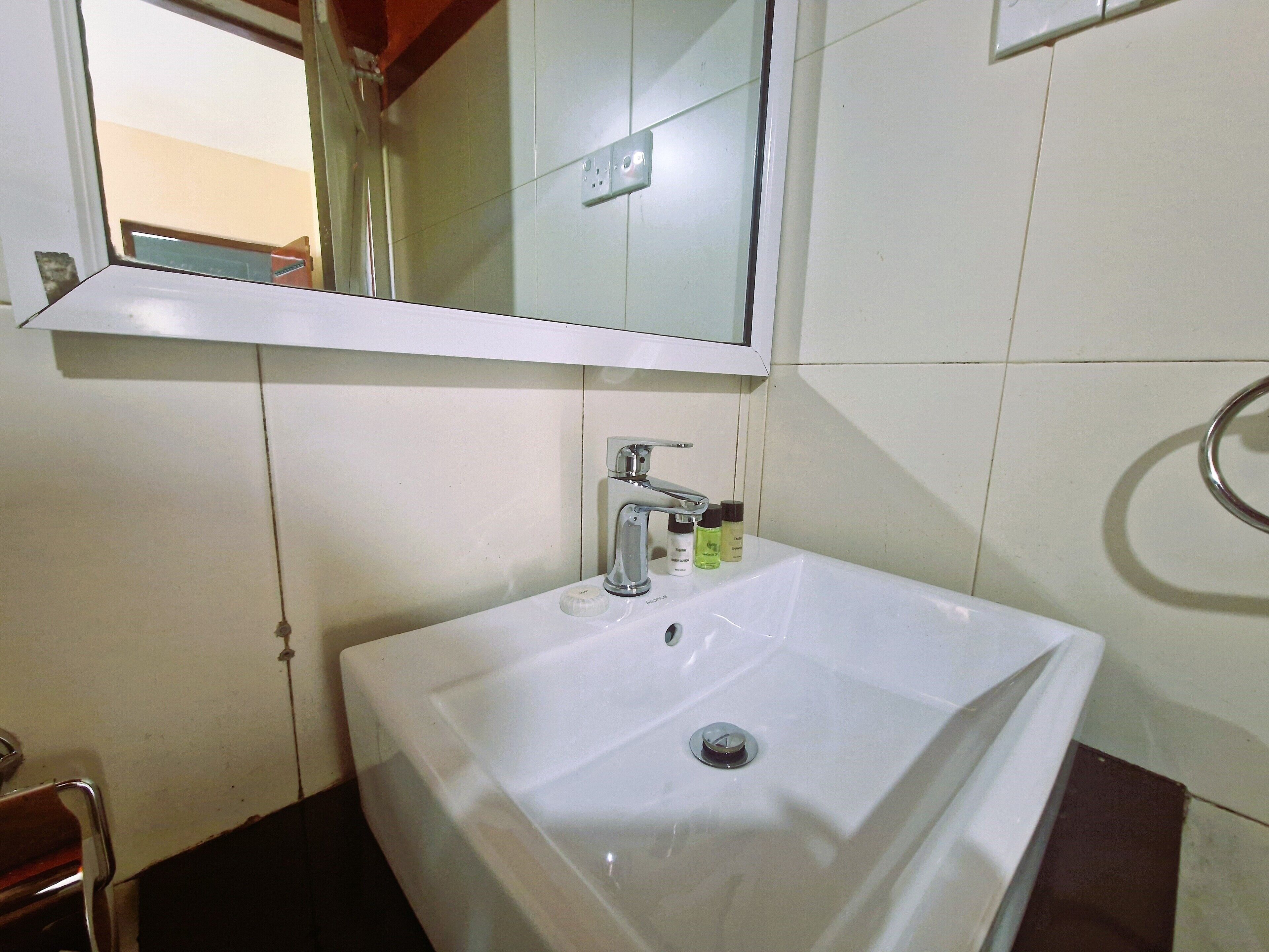 Un baño con un lavamanos blanco, un espejo encima y una zona de ducha visible a través de una ventana.