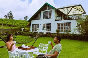 A two-story house with a green roof, large windows, and a garden with white chairs and tables. - The Tea Garden (Nuwara Eliya)