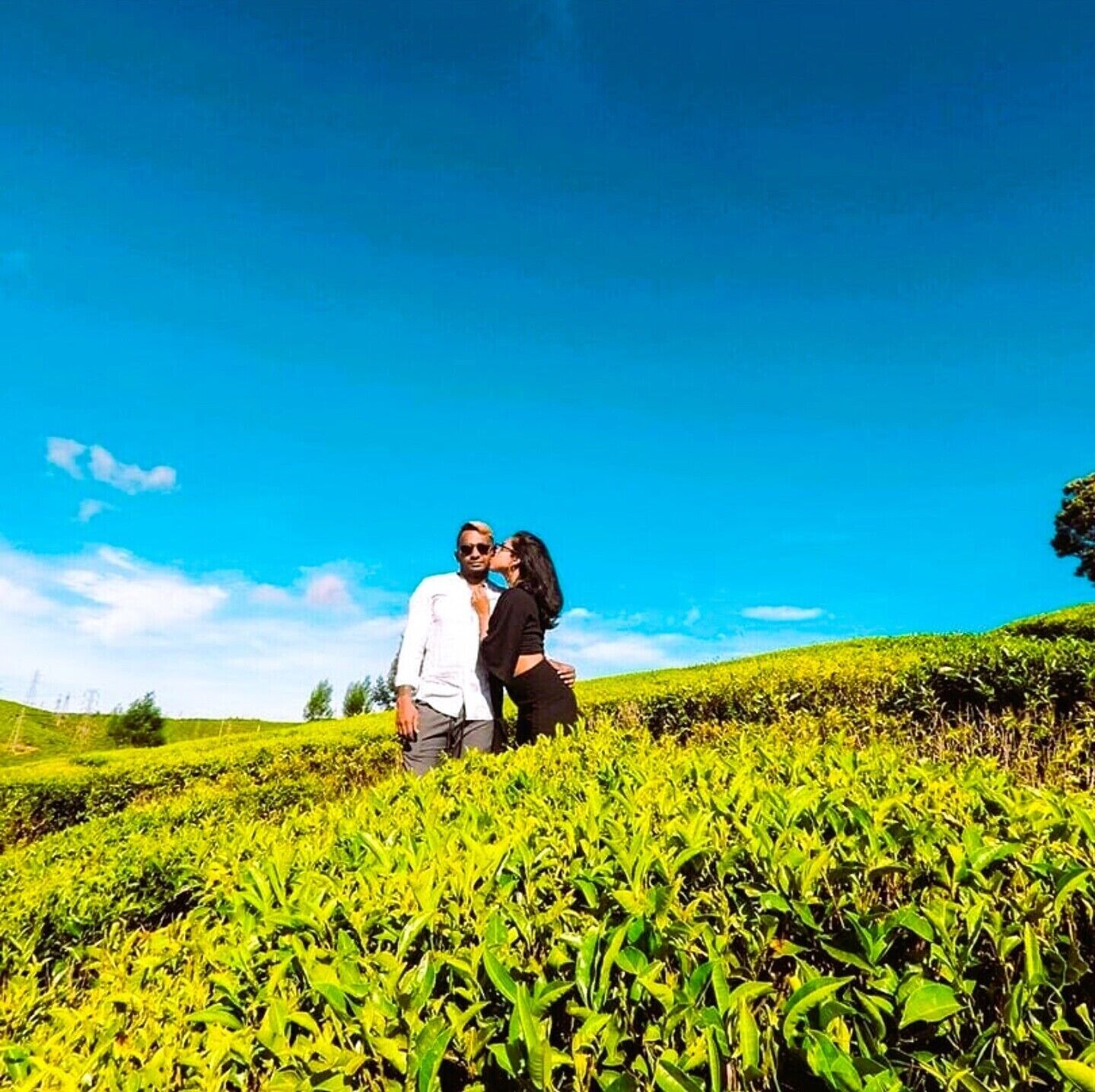 A couple standing in a lush green field with a clear blue sky.