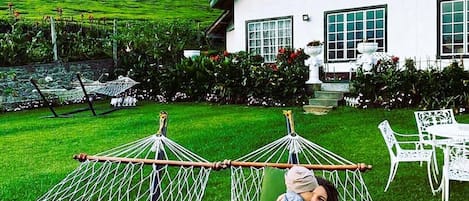 Una casa con un jardín amplio, una hamaca y muebles de exterior.