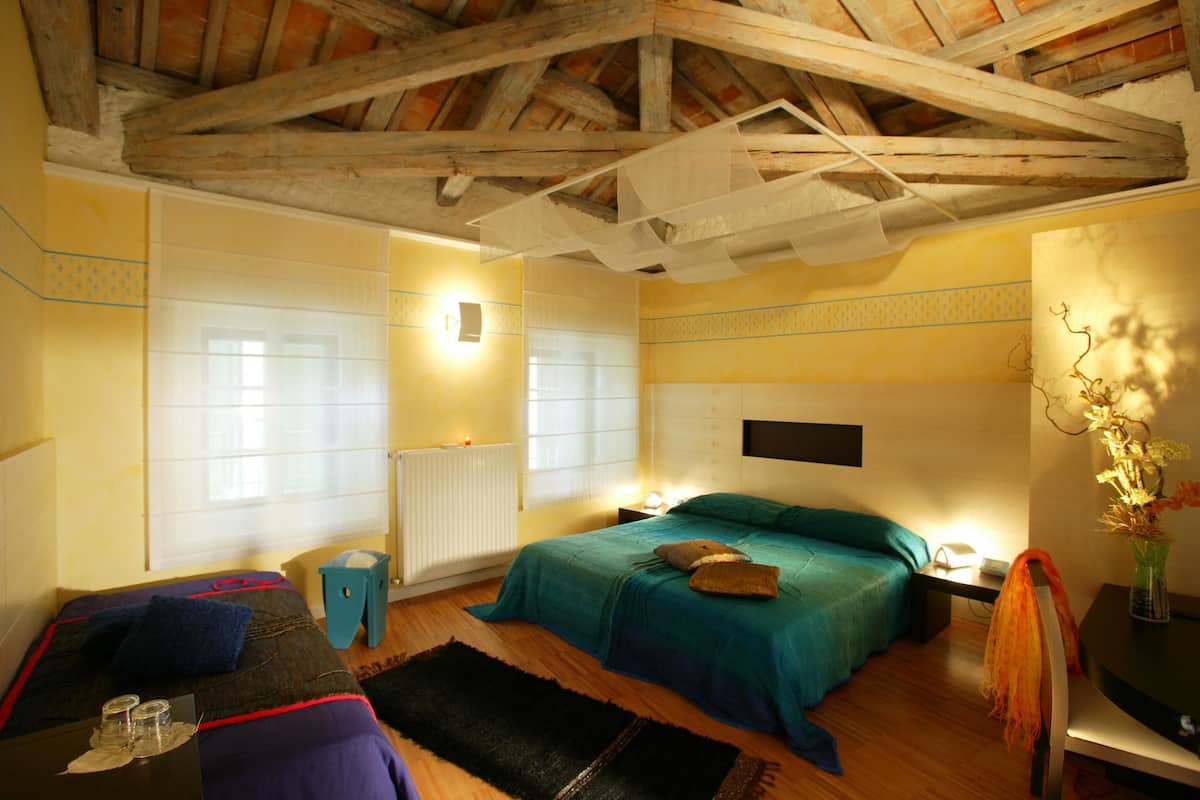 Una habitación con una cama, una mesita con vasos, una silla, un radiador y una ventana.