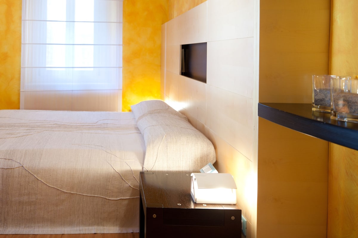 Una habitación de hotel con una cama, mesita de noche, lámpara y televisor montado en la pared.