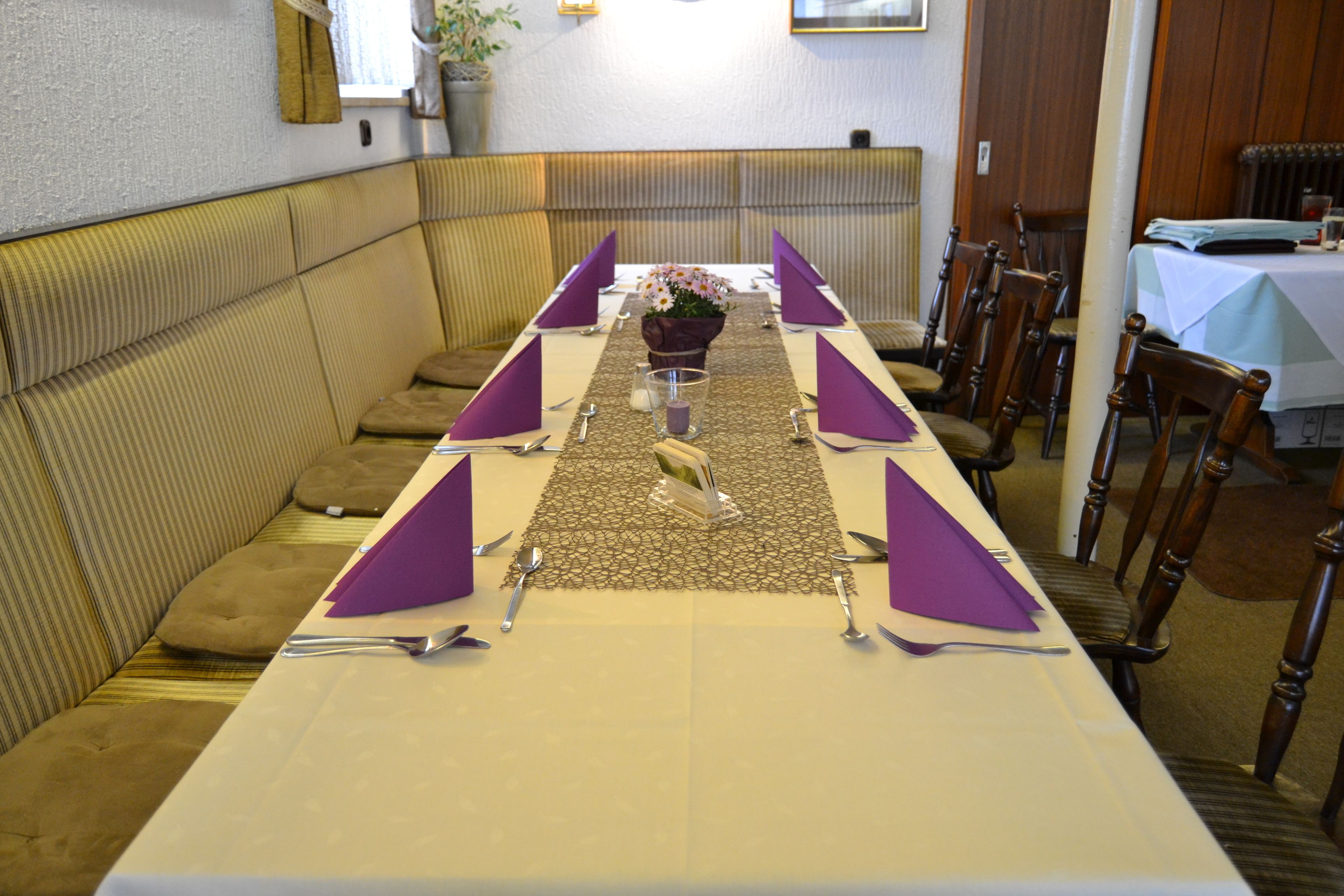 Una larga mesa de comedor con un arreglo floral central, rodeada de asientos acolchados y sillas de madera.