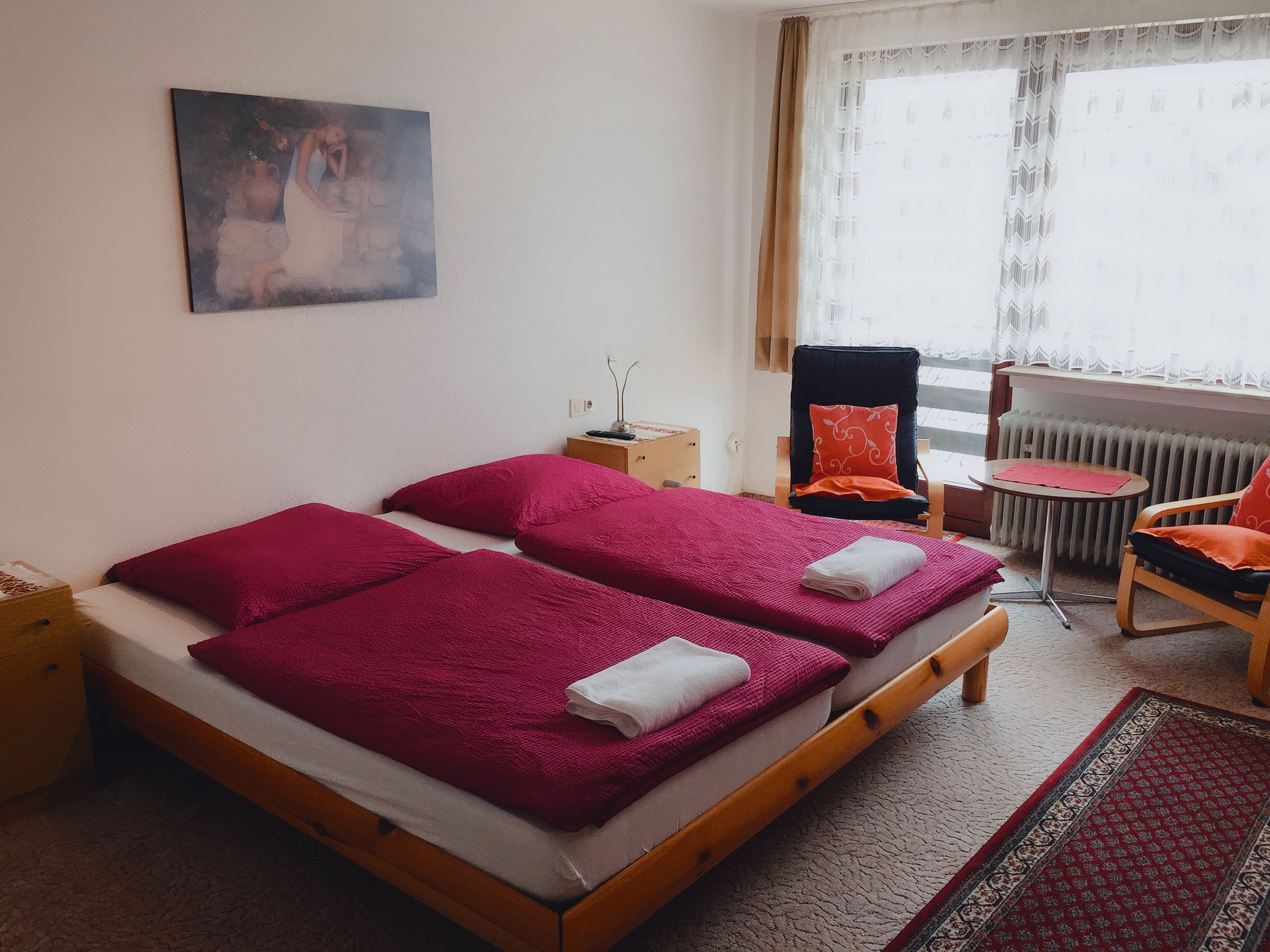 A bedroom with a bed, pillows, a chair, a table, and a radiator.