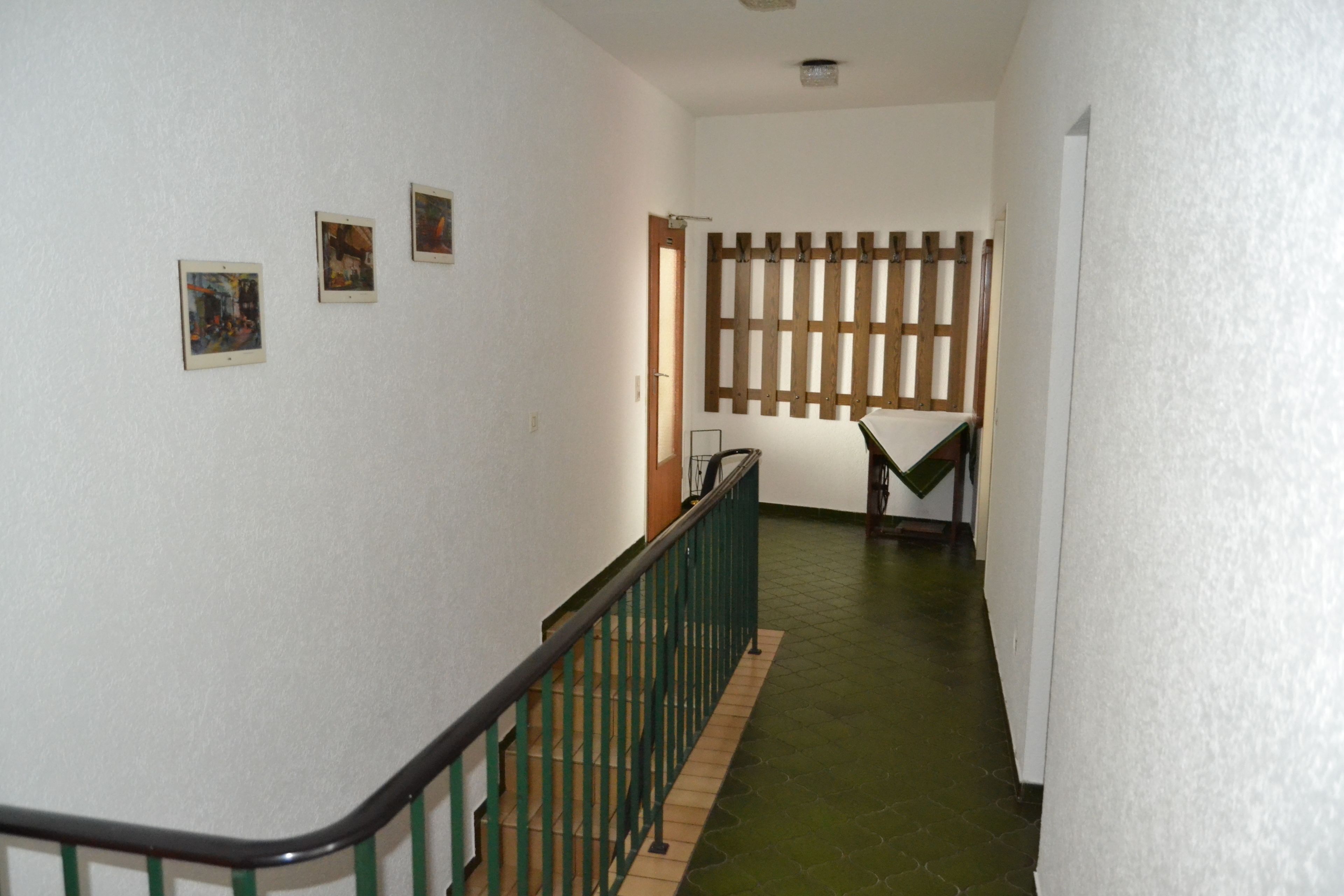 Um corredor com corrimão verde, parede de ripas de madeira e três quadros na parede.