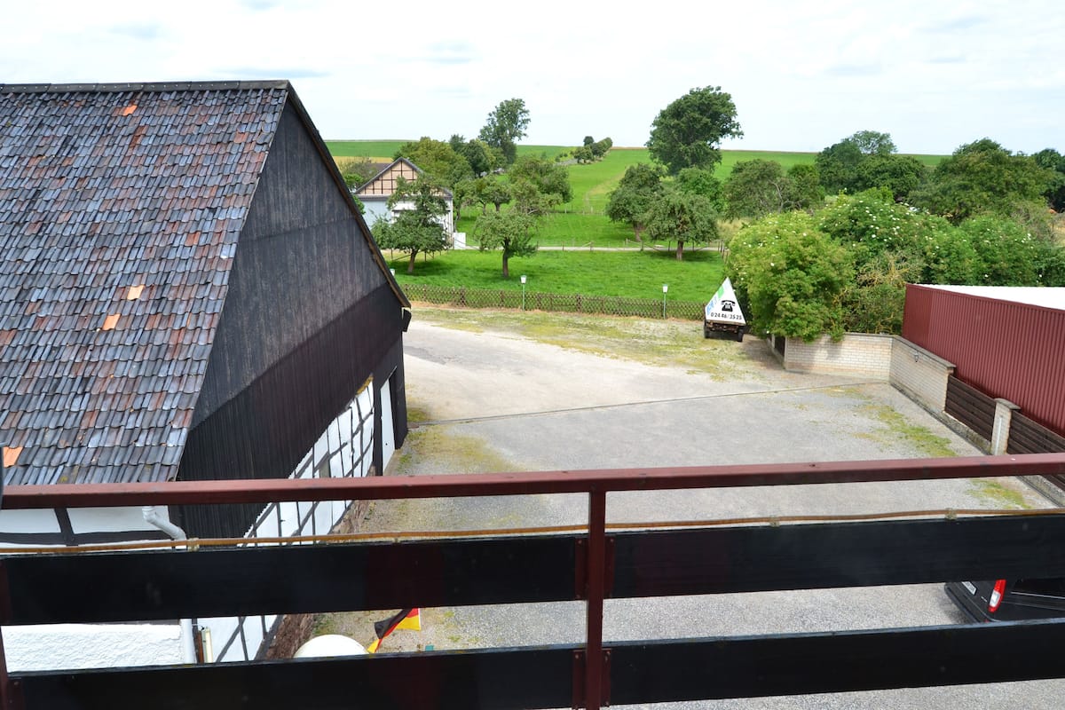 Uitzicht vanaf een balkon op een landelijk gebied, met een gebouw met een schuin dak, een omheind gebied en een weg met een verkeersbord.