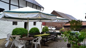 An outdoor patio with tables and chairs under umbrellas, a brick building in the background, and a car parked nearby. - Hotel Eifelhof Weina (Heimbach)