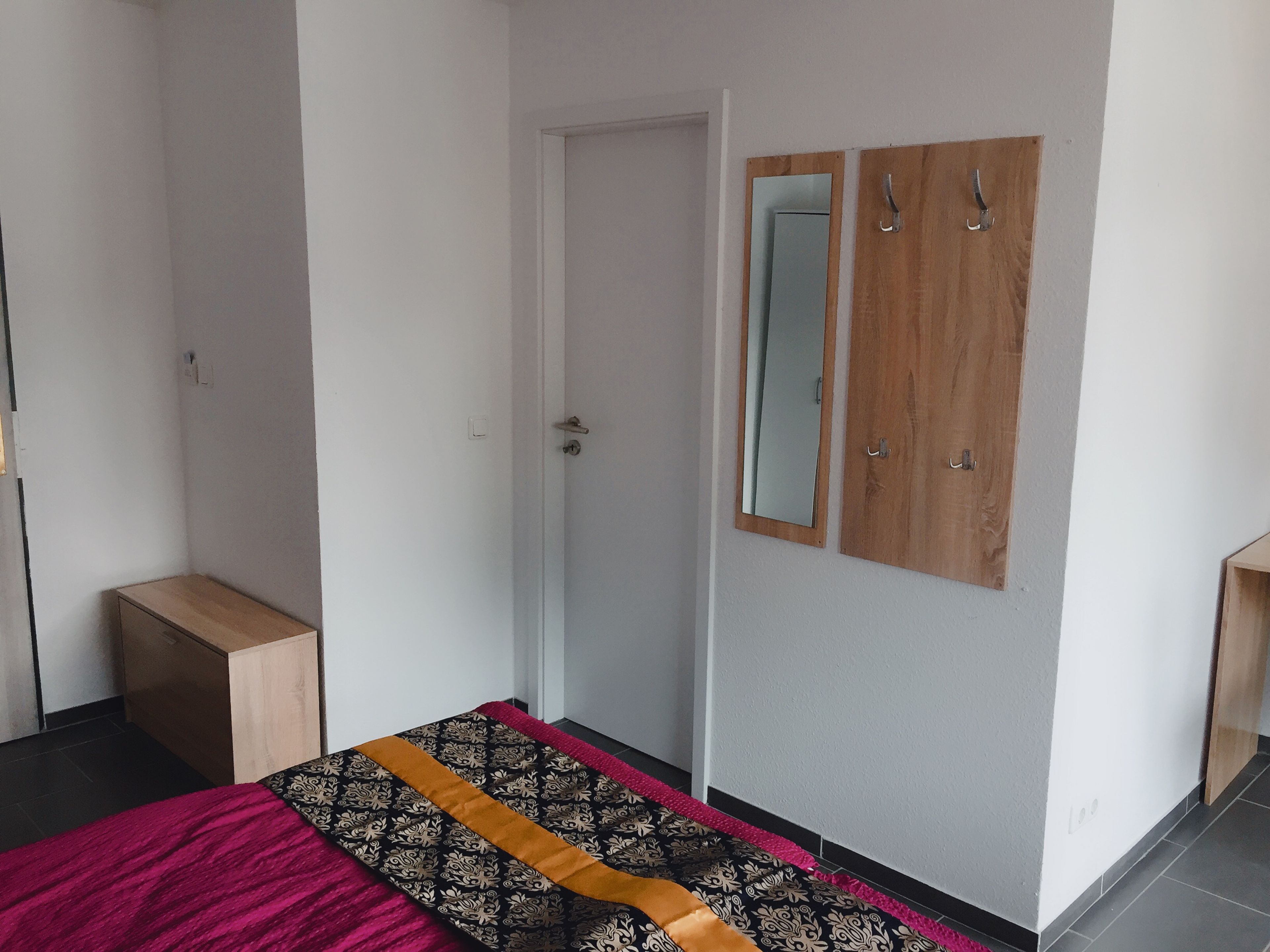 A bedroom with a bed, a wardrobe, a mirror, and a door.