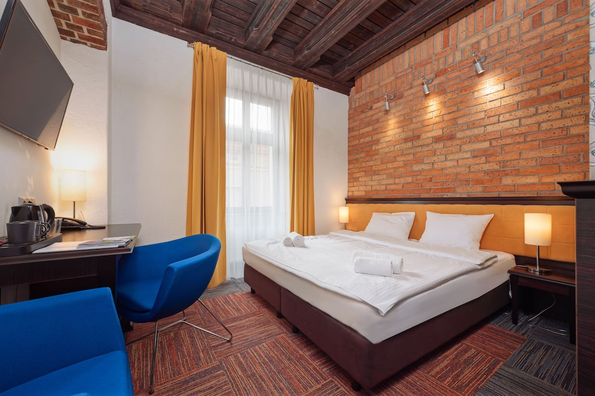 A hotel room with a bed, a desk with a computer, a chair, and a brick wall.