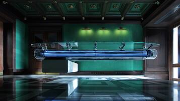 A room with a large glass coffin on a reflective floor, green walls, and a wooden ceiling with intricate designs.