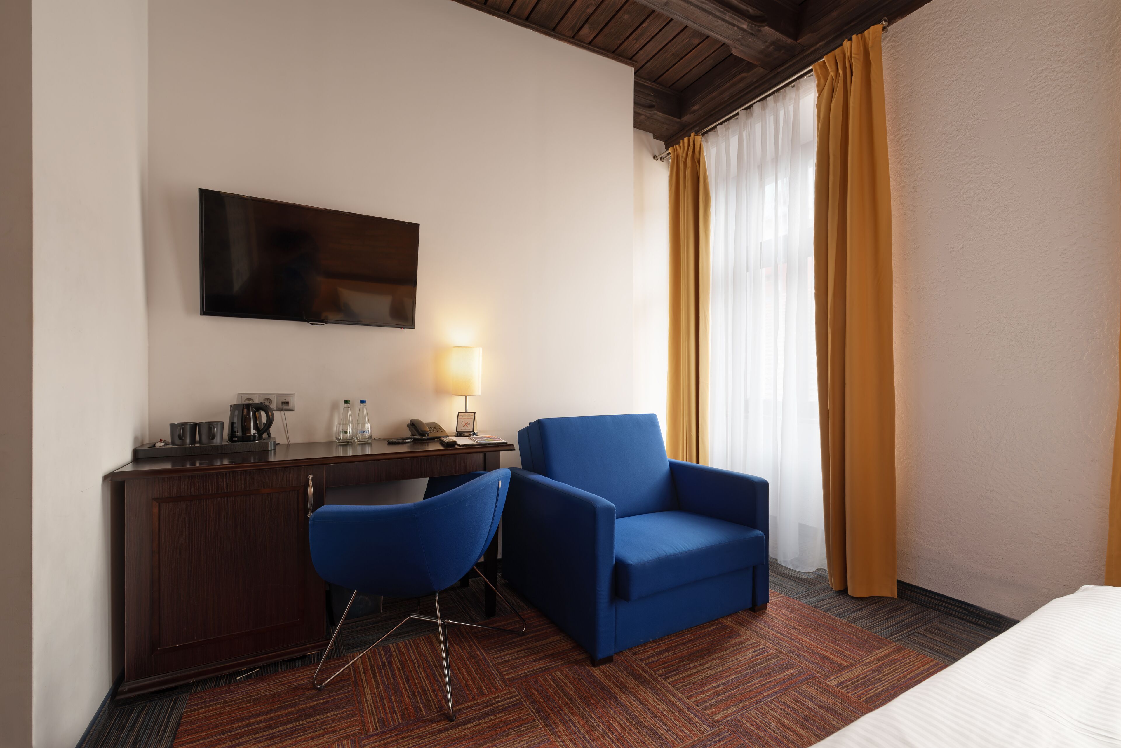 Ein Hotelzimmer mit Bett, Schreibtisch mit Stuhl, Flachbildfernseher, Lampe und einem Fenster mit Vorhängen.