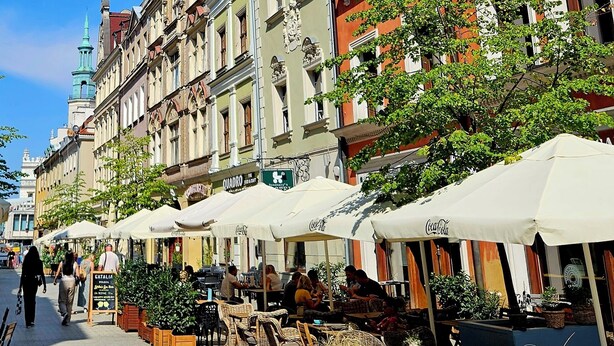 A street lined with historic buildings, outdoor seating areas, and a clear blue sky. - Palazzo Rosso Old Town (Poznan)