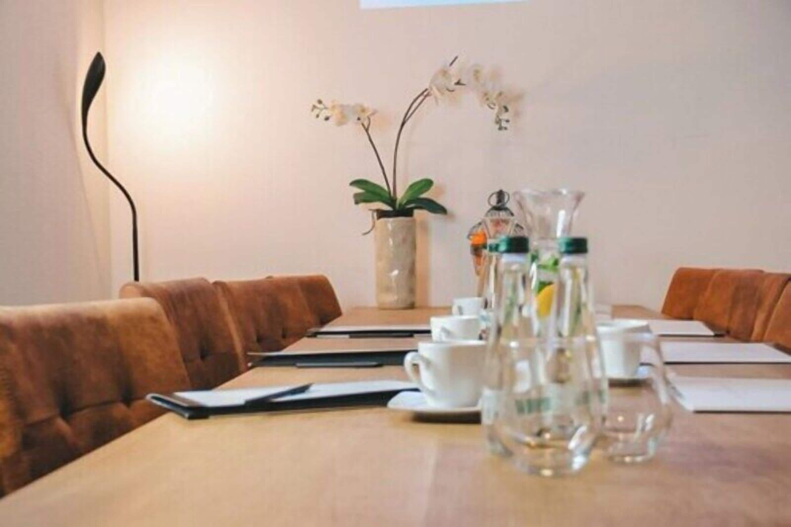 A conference room with a long table, brown leather chairs, white cups, and a vase with flowers.