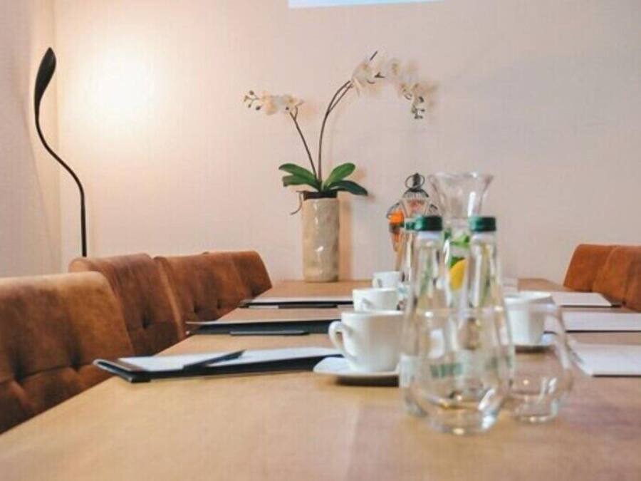 Ein Konferenzraum mit einem langen Tisch, braunen Ledersesseln, weißen Tassen und einer Vase mit Blumen.