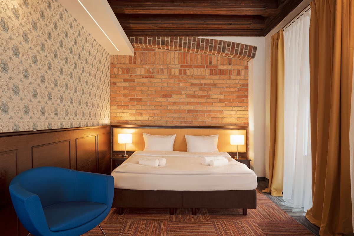 A hotel room with a brick-patterned headboard, a blue armchair, and a neatly made bed with towels.