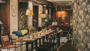 A dining area with a long table, chairs, and a sofa. There are plants and lamps. - Palazzo Rosso Old Town (Poznan)
