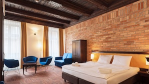 A hotel room with a brick wall, a large bed, two blue chairs, a wooden cabinet, and a carpeted floor. - Palazzo Rosso Old Town (Poznan)