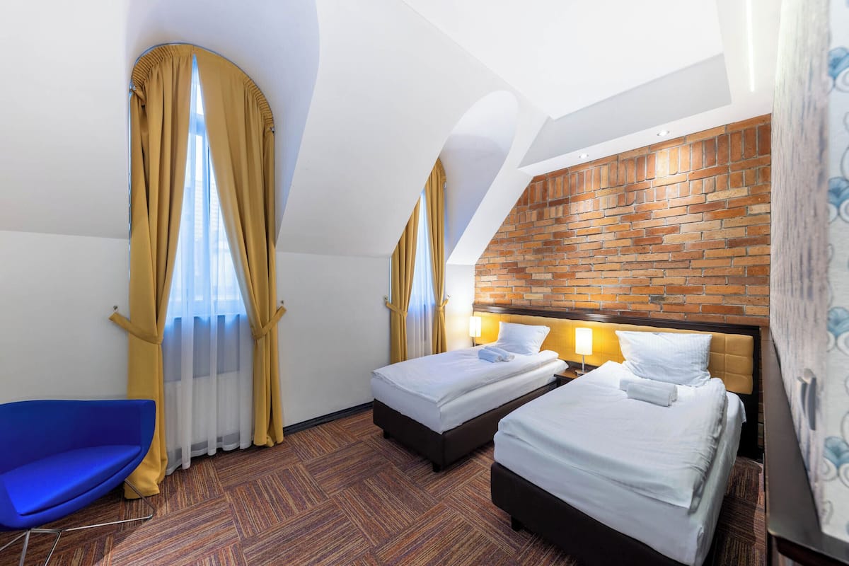 A hotel room with two beds, a blue chair, and a brick-patterned wall.