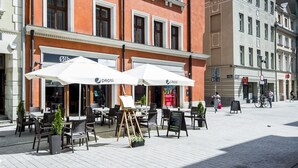 A building with a red facade, multiple windows, and outdoor seating with umbrellas. - Palazzo Rosso Old Town (Poznan)