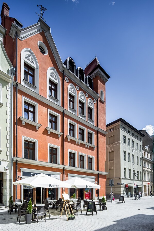 A building with a red facade, multiple windows, and outdoor seating with umbrellas. - Palazzo Rosso Old Town (Poznan)