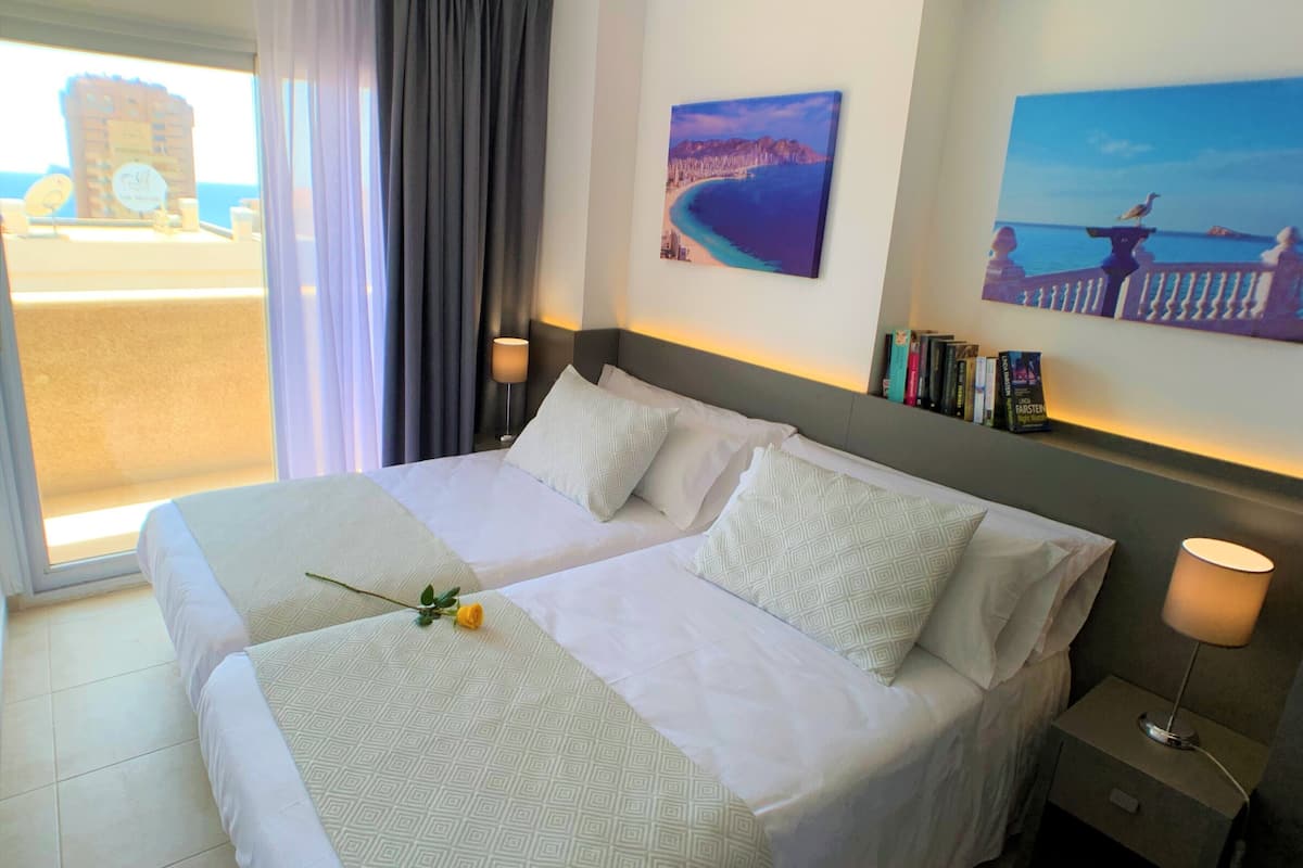 Habitación de hotel con una cama grande, dos mesitas de noche y vistas al mar a través de una ventana.