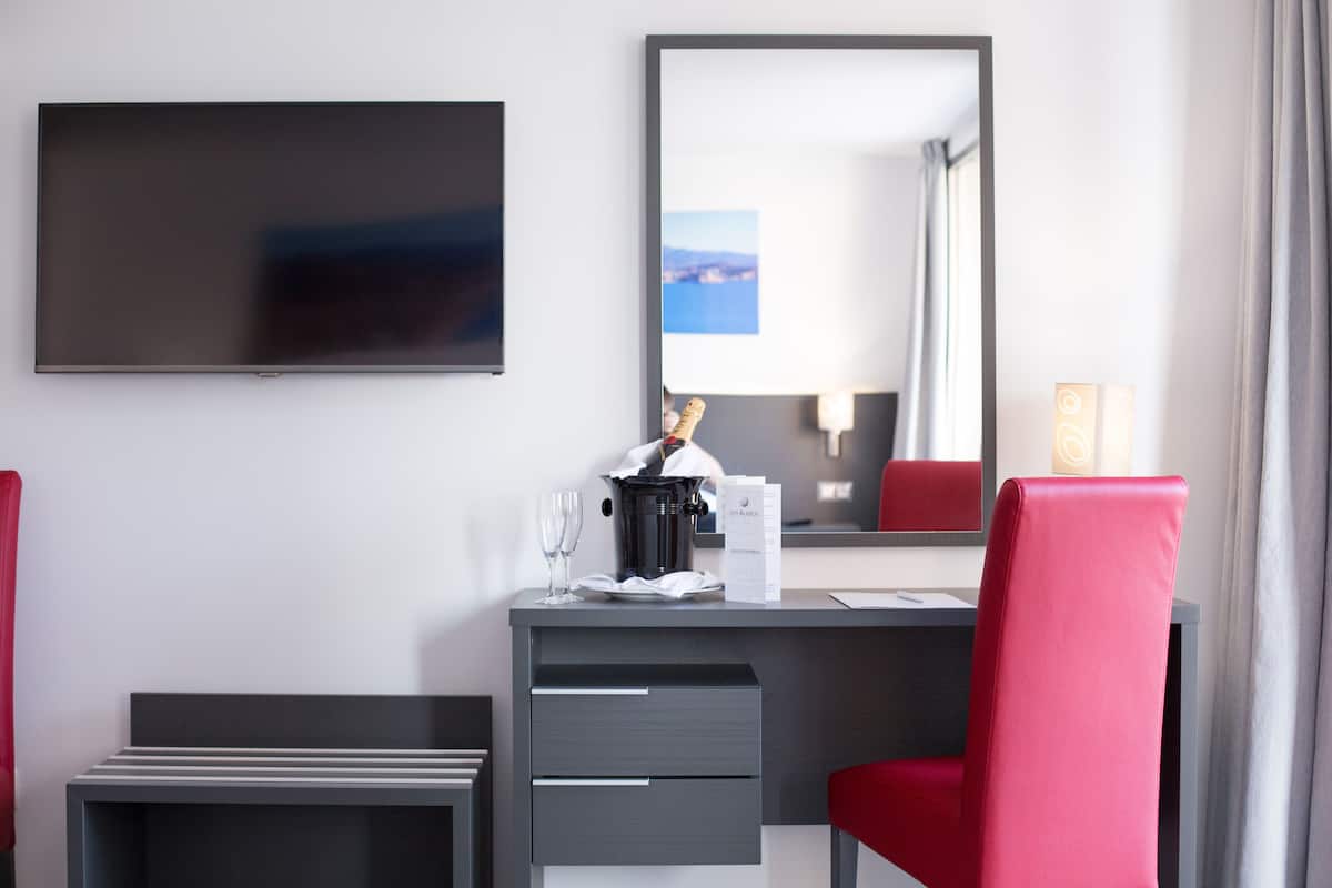 Habitación de hotel con televisión de pantalla plana, un escritorio con una silla roja, una botella de champán y un espejo grande.