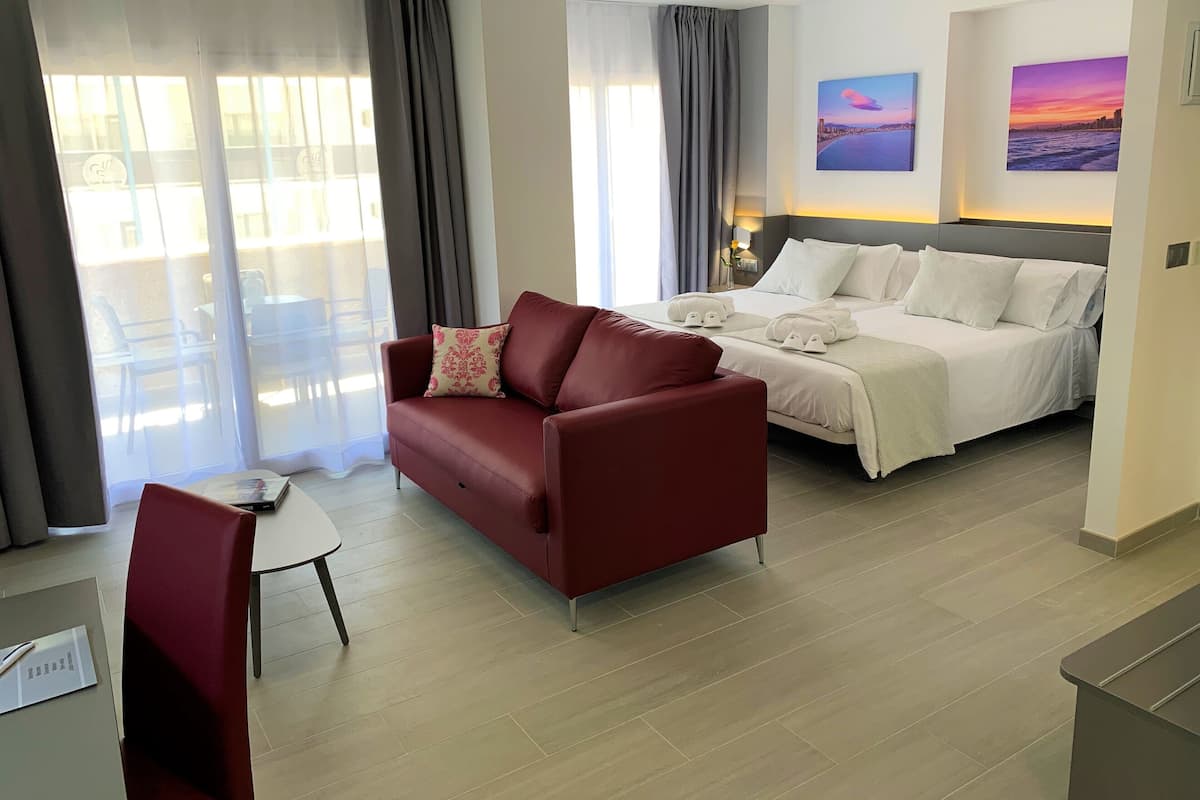 Una habitación de hotel con una cama, un sofá rojo, una mesita y una silla.