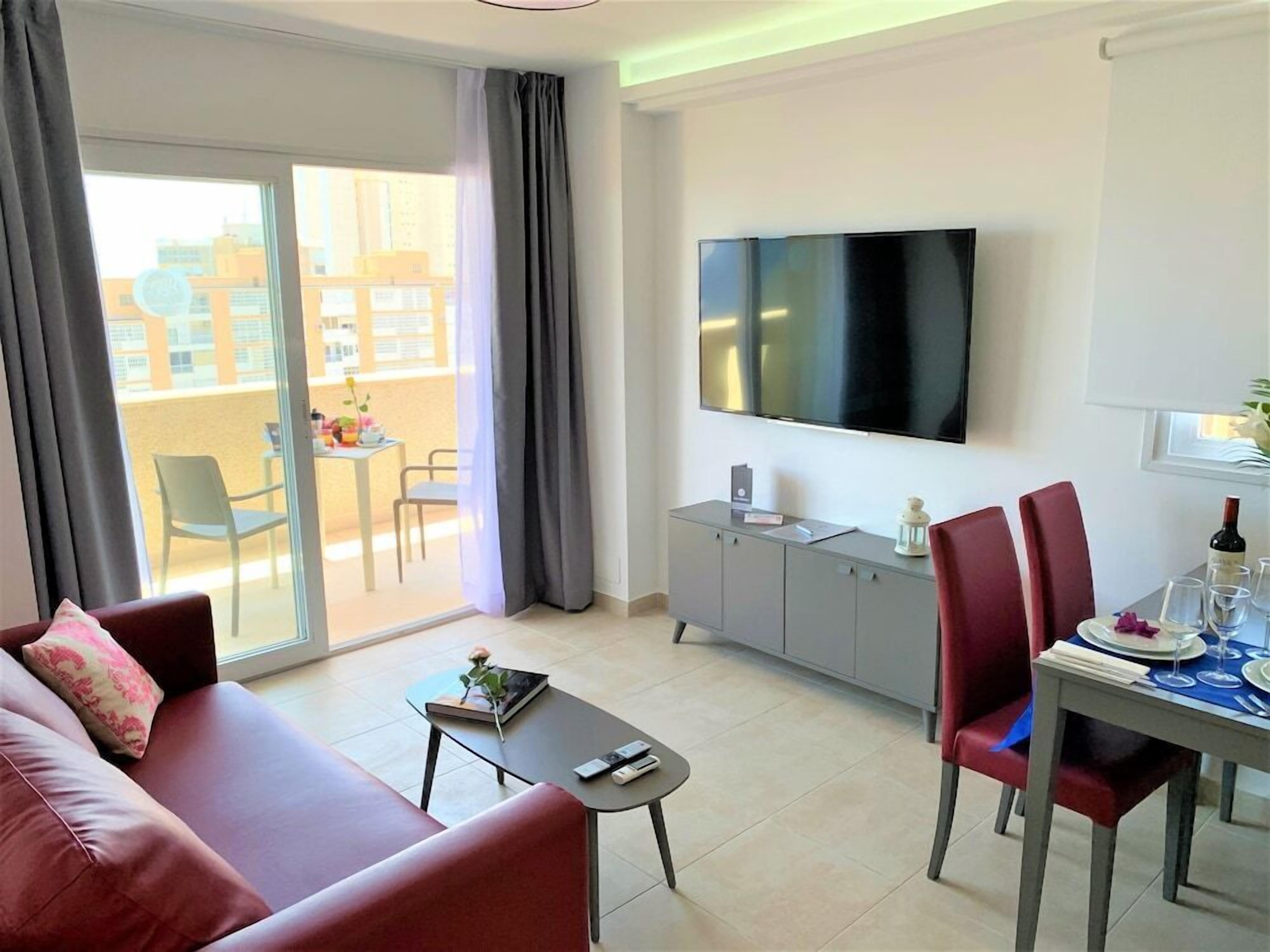Un soggiorno moderno con divano, tavolino, tavolo da pranzo con sedie, TV a parete e balcone con tavolo e sedie.